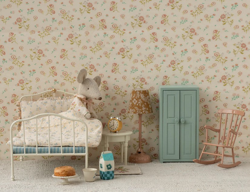 A cozy children's room with a white bed, a Maileg Mouse furniture set, stuffed mouse doll, miniature Maileg Side Table (Mouse) from Maileg, alarm clock, vintage lamp, mint wardrobe, pink rocker, and floral wallpaper with matching bedding.