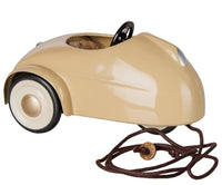A Maileg Car, Mouse - Wheat in beige from Maileg, featuring white wheels, a black steering wheel, and a brown pull string attached to the front—shown from a side view, perfect for imaginative play.
