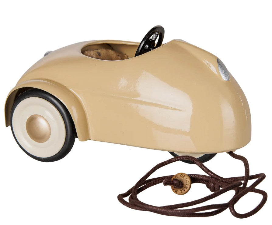 A Maileg Car, Mouse - Wheat in beige from Maileg, featuring white wheels, a black steering wheel, and a brown pull string attached to the front—shown from a side view, perfect for imaginative play.