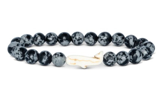 The Wayfare - Ocelli Stone Whale bracelet by fahlo features round, black and white speckled beads with a white whale-shaped charm—an ideal gift for marine life lovers.