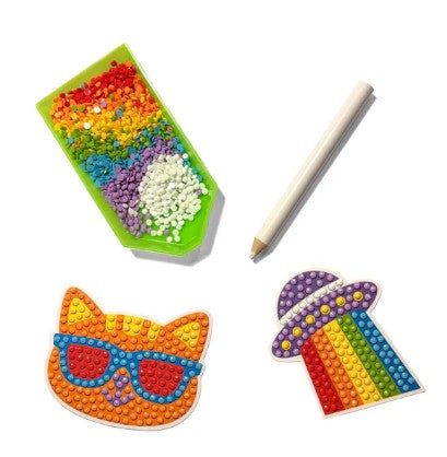 Get creative with the Ooly Mini Razzle Dazzle: D.I.Y. Gem Sticker Kit - Happy, a colorful kids’ craft set featuring a rainbow pencil, a cat face with sunglasses, and a UFO shooting rainbow rays—each design is ready to be jazzed up with round, raised gem stickers! The kit comes complete with unique sticker designs and a white stylus to help you apply the sparkling beads.