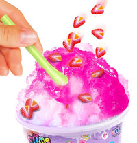 A hand stirs bright pink So Slime Ice Slime Mini Cup by License 2 Play with a green spoon, as heart-shaped strawberry pieces fall onto the slime, creating a moment of sensory fun reminiscent of playing with ice slime or mixing a mini slime cup.