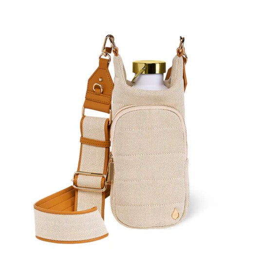 Introducing the Wader Full Brand HydroBag Handle Oatmeal Canvas—a beige crossbody bag featuring a wide adjustable strap, convenient front pocket, and dedicated water bottle holder. It comes complete with a white bottle topped with a gold cap, making it the perfect hydration accessory for your daily adventures.