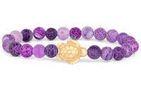 The fahlo Journey - Coral Reef Violet Sea Turtle bracelet features round purple and lavender marbled beads with a cream turtle centerpiece—ideal for ocean conservation enthusiasts.