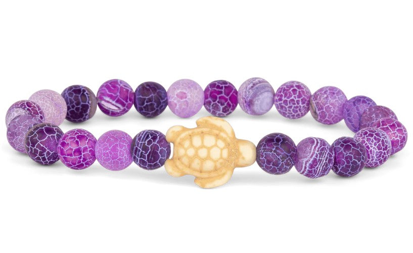 The fahlo Journey - Coral Reef Violet Sea Turtle bracelet features round purple and lavender marbled beads with a cream turtle centerpiece—ideal for ocean conservation enthusiasts.