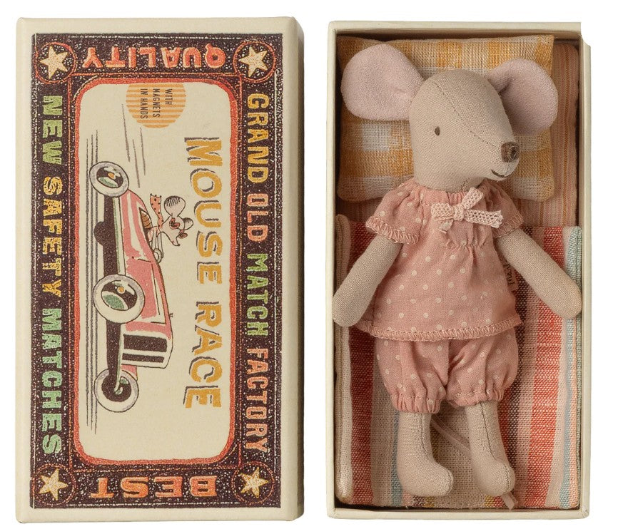 The Maileg Big Sister Mouse In Matchbox by Maileg features a small mouse in pink pajamas lying in a matchbox bed decorated with “Mouse Race,” “Grand Old Match Factory,” and a colorful racing car illustration.