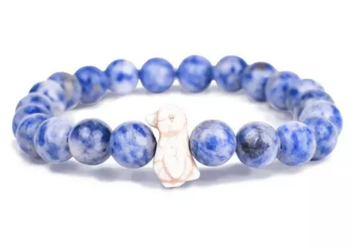 The Passage - Igloo Blue Penguin bracelet by fahlo features round blue marbled beads and a single white rabbit-shaped bead, displayed on a white background—great for wildlife conservation fans or as a unique penguin-themed accessory.