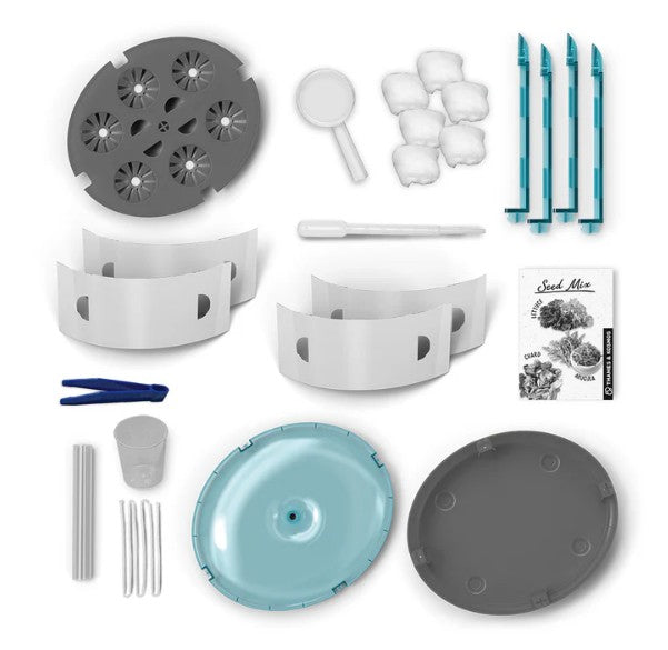 The Thames & Kosmos Hydroponics Lab is shown, featuring white and gray plastic components, blue support stakes, seed packets, cotton packs, a pipette, tweezers, a small measuring cup, and a turquoise lid—all organized on a white background. This complete set makes an ideal STEM kit for hands-on learning with your own hydroponics lab.