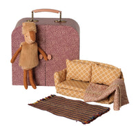 The Maileg Reindeer in Suitcase, Little Sister, is displayed alongside a patterned suitcase, a yellow patterned sofa, a coordinating blanket, and a striped rug—all from the Maileg collection—creating a cozy miniature living room scene that inspires travel-themed imaginative play.