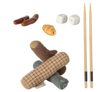The Maileg Bonfire Set, Mouse by Maileg features assorted miniature food items and two chopsticks, ideal for camping play or a mice bonfire set. Includes sausage-like pieces, marshmallows, pastry, and patterned fabrics for realistic camp treats.