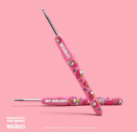 Two pink crochet hooks from the Woobles My Melody Crochet Kit are shown on a pink background, featuring My Melody and Sanrio characters, with "WOOBLES" and "MY MELODY" on the handles.