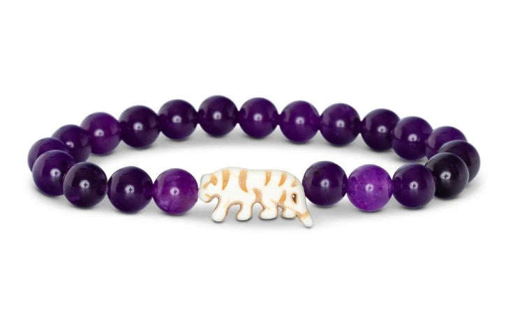 Introducing the Prowl - Royal Purple bracelet by fahlo: a beaded conservation piece featuring round, purple amethyst stones and a central white bead shaped like a tiger with gold stripes, designed to inspire awareness and support wildlife causes through the fahlo app.
