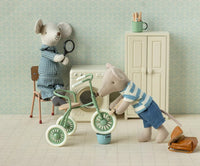 The Maileg Tricycle Mouse, Big Brother - Brown sits in a miniature room with his tricycle and accessories—cabinet, mug, and bag—creating a charming pretend play scene from Maileg.
