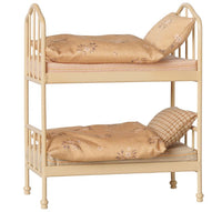 The Maileg Bunk bed, Mouse - Wheat by Maileg is a small beige metal bunk bed featuring ornate rails and delicate four rounded legs. Each level comes complete with a mattress, pillow, blanket, and beautiful gold and floral bedding—perfect for outfitting your mouse house in style.