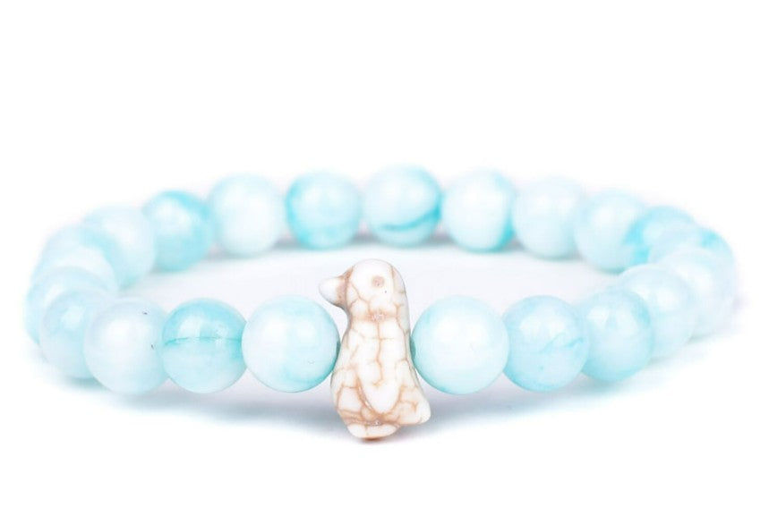 The fahlo Passage - Seafoam Penguin bracelet features round, light blue beads and a single cream-colored penguin bead at the center, inspired by wildlife conservation.