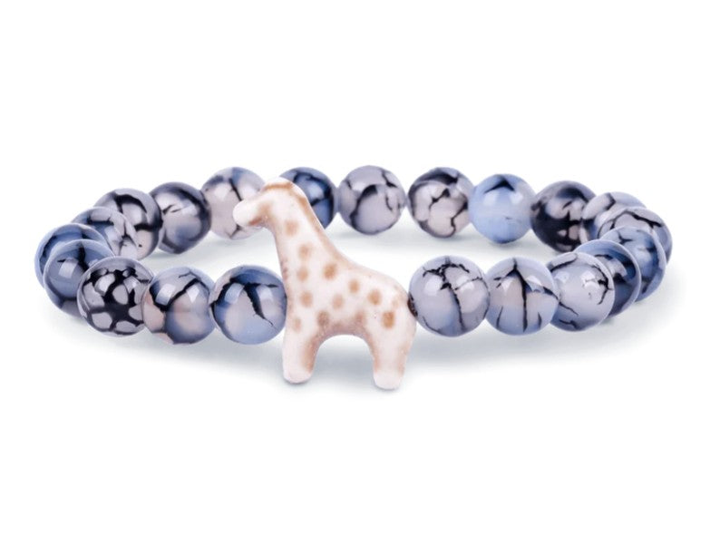 The fahlo Trek - Keystone Giraffe bracelet features round blue and white marbled beads with a ceramic giraffe charm, offering a playful accessory inspired by giraffe conservation.