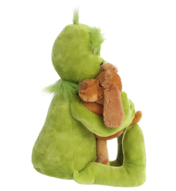 The Aurora Holiday Hugs features a green plush toy resembling the Grinch hugging a brown plush dog, both sitting side by side and seen in profile—a heartwarming, cuddly duo that makes the perfect holiday gift for any festive plush collector.