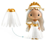 The DJECO Tinyly Marguerite & Leopold figurine features long white hair and wears a detachable white dress with gold accents that resembles flower petals, as highlighted by an arrow indicating the removable skirt. This miniature collectible from DJECO comes with a gold and white accessory, making it perfect for imaginative play.