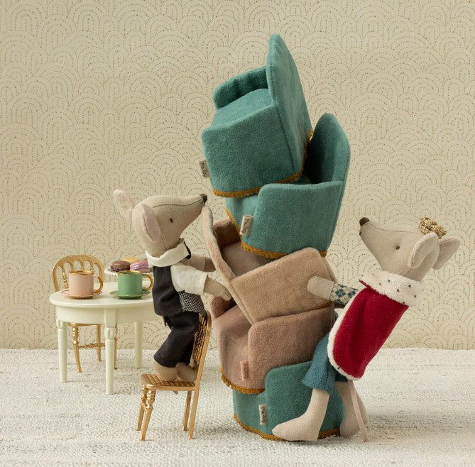 Maileg's King Mouse, Dad, in regal attire balances stacked cushions, creating a fairy-tale scene with a tiny tea table and chairs against a patterned wall.