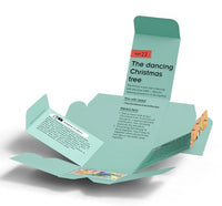 A light green, partially open cardboard box from Thames & Kosmos displays printed instructions and vibrant graphics. The text highlights "Day 23: The Dancing Christmas Tree" and details the required materials and steps for an interactive experiment, all as part of The Thames & Kosmos Science Advent Calendar packed with engaging STEM activities.