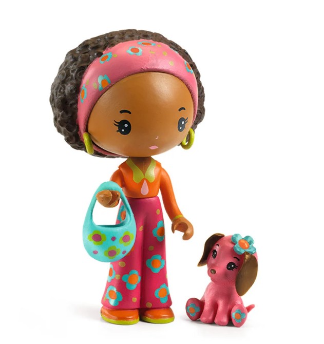 The DJECO Tinyly Poppy & Nouky set features a charming DJECO figurine with brown skin, curly hair adorned with a pink headband, an orange flowered outfit, and green earrings, holding a blue bag next to a small pink dog with brown ears and a blue flower on its head—perfect for imaginative play or adding to your collectible figure set.