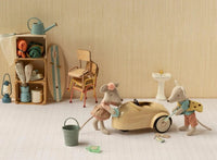Two Maileg mice, including the Maileg Driver Mouse, Little Sister, engage in imaginative play as they clean a miniature transportation-themed toy car in a charmingly detailed room. In the background are a shelf, chair, and sink, accompanied by thoughtful little props like a watering can, towels, and a skateboard.