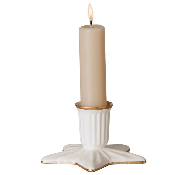 A lit beige candle sits in the Maileg Candle holder, Star, Large—a white ceramic star-shaped holder with gold-trimmed edges from Maileg.