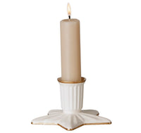 A lit beige candle sits in the Maileg Candle holder, Star, Large—a white ceramic star-shaped holder with gold-trimmed edges from Maileg.