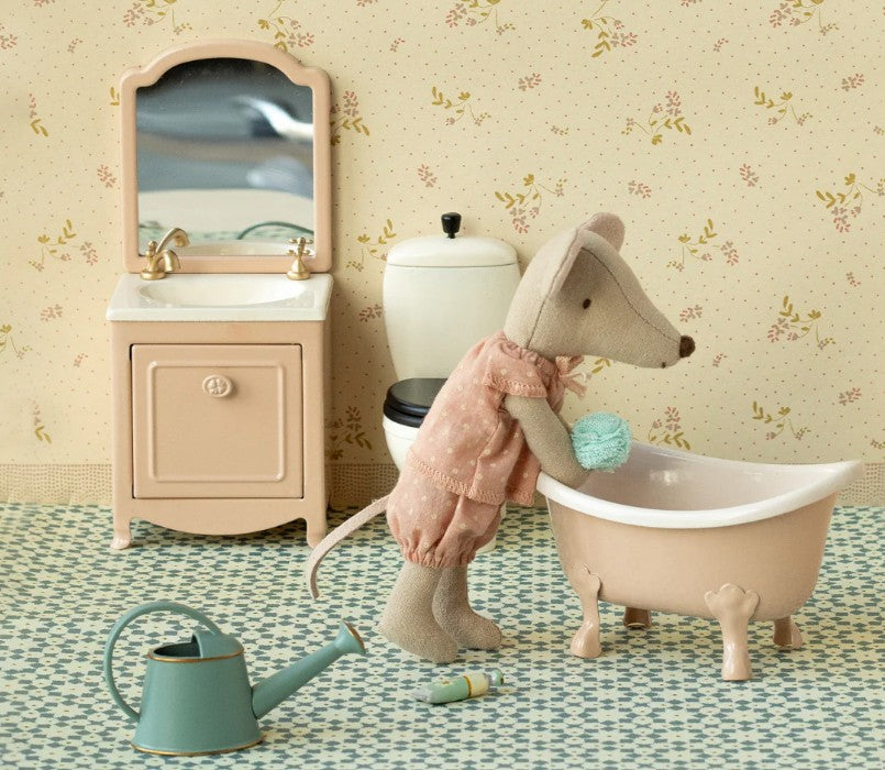 A Maileg mouse in pajamas stands by the Maileg Bathtub, Mouse - Rose with a sponge, in a miniature bathroom featuring a sink, toilet, watering can, and floral wallpaper.