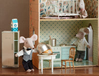 A dollhouse kitchen scene with Maileg Side Table, Mouse by Maileg, two mouse dolls as chef and server at the table, a fridge labeled MILK, and a third mouse doll in a crib upstairs—ideal for creative dollhouse decorating.