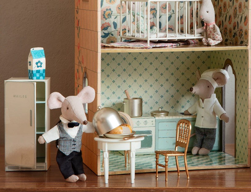 A dollhouse kitchen scene with Maileg Side Table, Mouse by Maileg, two mouse dolls as chef and server at the table, a fridge labeled MILK, and a third mouse doll in a crib upstairs—ideal for creative dollhouse decorating.
