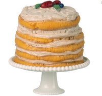 The Maileg Party Cake And Cake Stand, Mouse - Off White by Maileg features a layered sponge cake with white frosting and colorful fruit on top, set on a white pedestal stand—ideal for any dollhouse party.