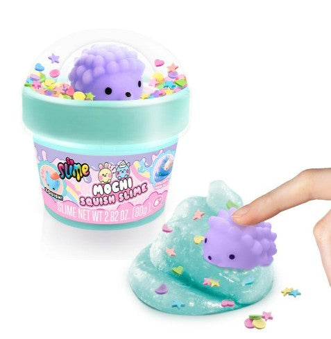 A cute purple hedgehog toy rests on sparkling blue So Slime Mochi Slime by License 2 Play, topped with star confetti for sensory play and stress relief. Someone presses the soft, squishy Mochi slime, enjoying its soothing texture. The nearby container is labeled “So Slime Mochi Slime” from License 2 Play and features colorful decorations.