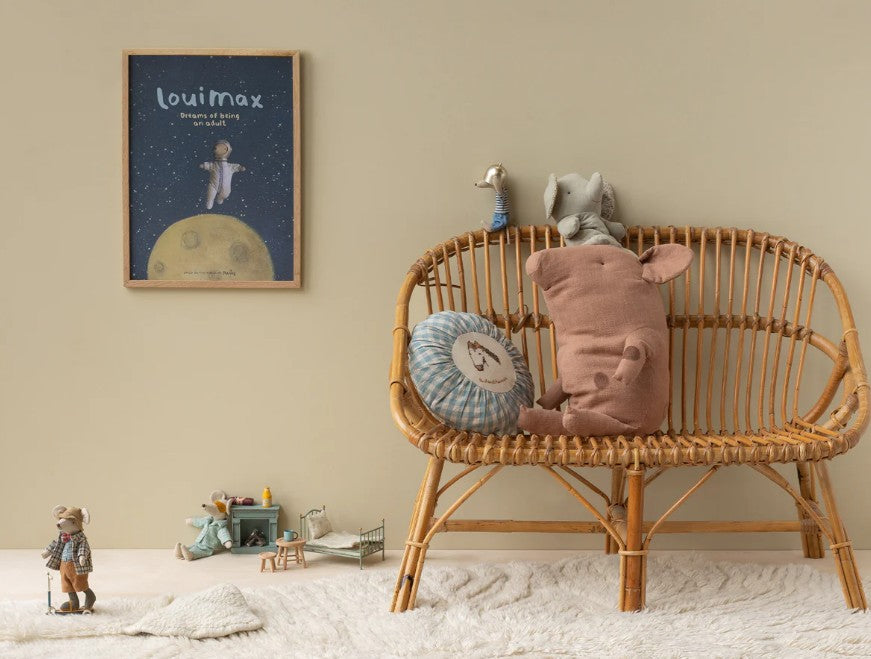 A cozy kids’ room features a rattan bench with the Maileg Granddad Mouse plush by Maileg, a space-themed poster on the wall, toy animals on a soft rug, and a miniature table and chair set in the corner.