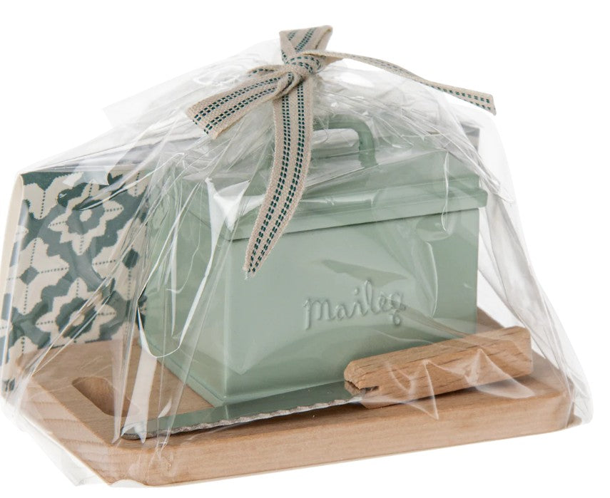 The Maileg Bread Box W. Utensils, Miniature by Maileg—featuring a green tin box and utensils—is a charming furniture accent for your Maileg Mouse, neatly wrapped in clear plastic with a ribbon on top.