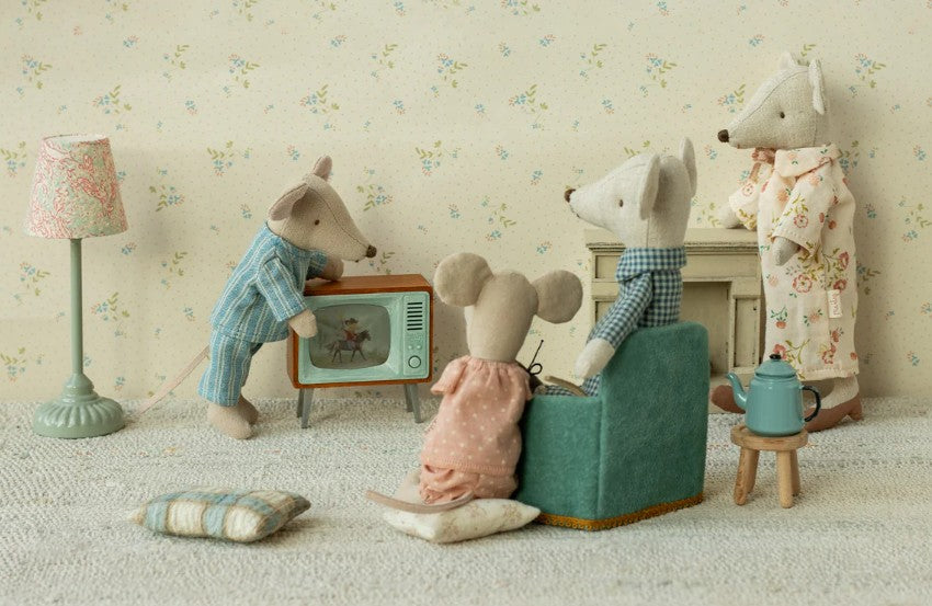 Four Maileg mice in pajamas relax in a cozy living room with the Maileg Television, Mouse, plus a lamp, pillows, and teapot—an adorable Maileg accessory for any dollhouse.