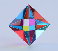 The Aether by CMY Cubes is a colorful, geometric diamond-shaped sensory display with a reflective, symmetrical pattern—perfect for stress relief. Set against a light blue background, it showcases vibrant hues to soothe and captivate.