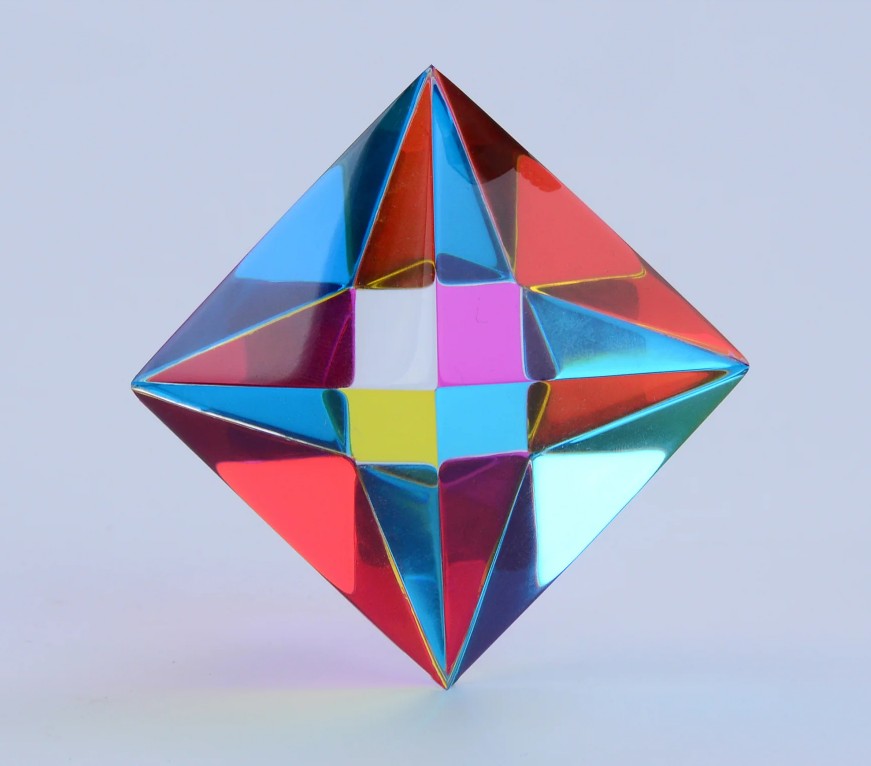 The Aether by CMY Cubes is a colorful, geometric diamond-shaped sensory display with a reflective, symmetrical pattern—perfect for stress relief. Set against a light blue background, it showcases vibrant hues to soothe and captivate.
