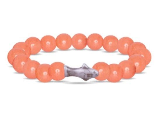 The Voyage - Sunrise Glow Shark bracelet by fahlo features round, coral-colored beads and a gray shark charm—ideal for marine conservation fans or anyone seeking a unique shark tracking accessory.
