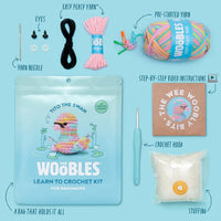 The Woobles Tito the Swan Pastel Crochet Kit for beginners includes a resealable bag with a swan image, colorful yarn, crochet hook, stuffing, plastic eyes, yarn needle, pre-started yarn, video instructions, and a small box.
