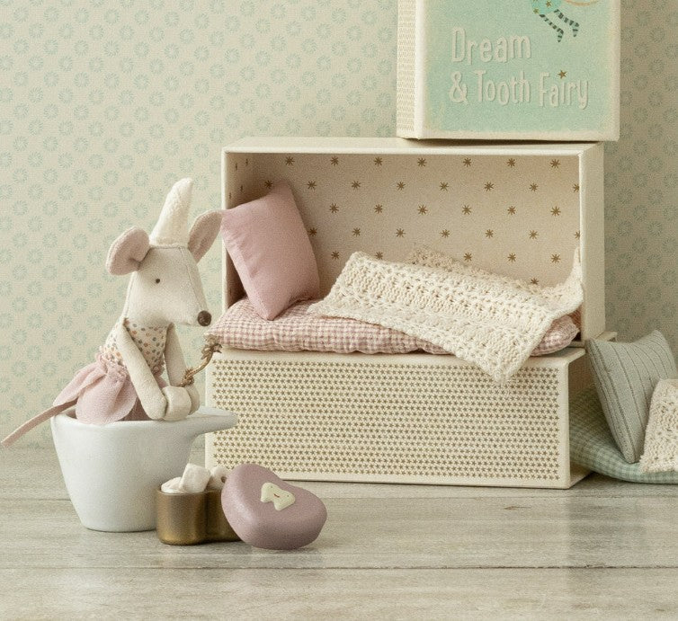 The Maileg Tooth Fairy Mouse, Little Sister in Matchbox by Maileg wears a pink dress and sits with her matchbox bed, pillows, blanket, a heart-shaped box, and a “Dream & Tooth Fairy” book beside her.
