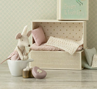 The Maileg Tooth Fairy Mouse, Little Sister in Matchbox by Maileg wears a pink dress and sits with her matchbox bed, pillows, blanket, a heart-shaped box, and a “Dream & Tooth Fairy” book beside her.
