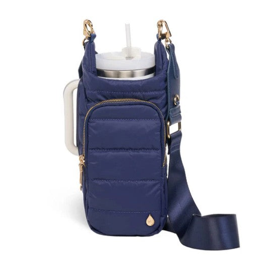 A navy blue Wander Full Brand HydroBag insulated drink carrier—with a zippered front pocket, gold hardware, an adjustable shoulder strap, and the convenient HydroBag Handle Navy for easy carrying—holds a large cup with a lid and straw.