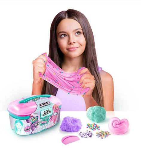 A girl stretches pink slime with colorful beads from the Craze Sensations ASMR Mixin Sensations Caddy by License 2 Play, surrounded by slime containers, a palette, foam balls, and more slime on a white surface—perfect for sensory exploration and ASMR play.