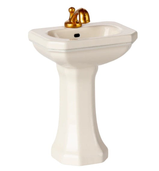 The Maileg Bathroom Sink, Mouse - Off white by Maileg features a small pedestal design with a shiny gold faucet, making it perfect for completing your Maileg mice setup. It is photographed against a plain white background.