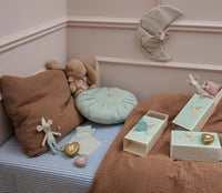 A cozy children’s room with a brown pillow, mint round cushion, plush bunny, Maileg Tooth Fairy Mouse, Little Brother in Matchbox by Maileg, pastel storage boxes, heart trinkets, and a fabric moon above a striped bed for imaginative play.