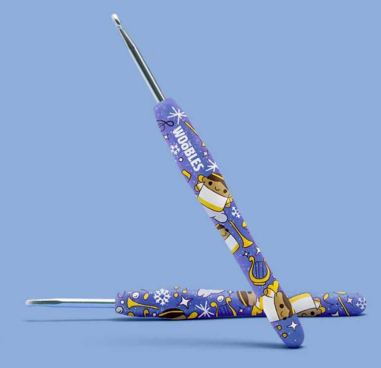 Two blue-handled crochet hooks, featuring cartoon animals, snowflakes, and "WOOBLES," are shown on a light blue background—perfect for beginners using The Woobles Claire the Angel Crochet Kit.