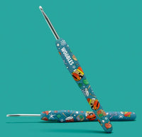 Two colorful crochet hooks with playful, cartoon-style designs and "WOBBLES" on one handle, from The Woobles Hazel the Nutcracker Crochet Kit, shown on a solid teal background—perfect for any beginner crochet kit.