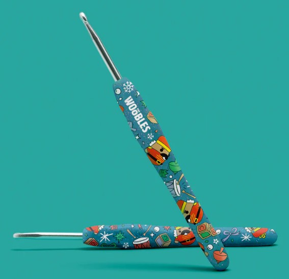 Two colorful crochet hooks with playful, cartoon-style designs and "WOBBLES" on one handle, from The Woobles Hazel the Nutcracker Crochet Kit, shown on a solid teal background—perfect for any beginner crochet kit.