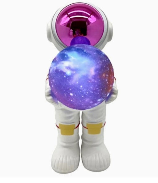Introducing the Fahionit Astronaut Wireless Speaker—a unique astronaut-themed decor piece featuring a small astronaut figurine with a shiny pink visor holding a round speaker adorned with a vibrant galaxy pattern. Perfect for adding an out-of-this-world accent to your space!.